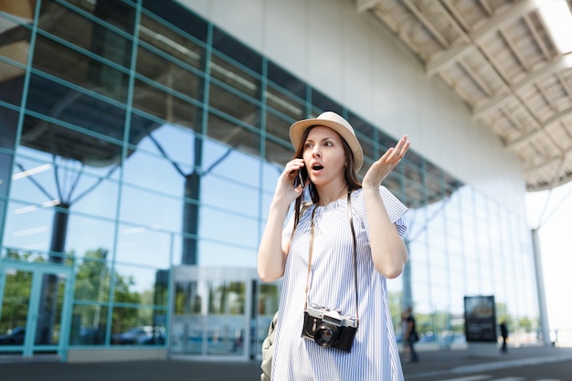 Femme touristique voyageuse choquée avec un appareil photo rétro vintage écartant les mains pour parler à un ami d'appel de téléphone portable