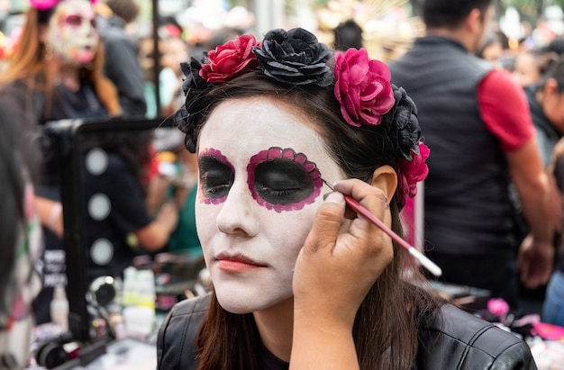 Photo femme en train d'être convertie en catrina avec un diadème rose dans le jour traditionnel des morts à mexico