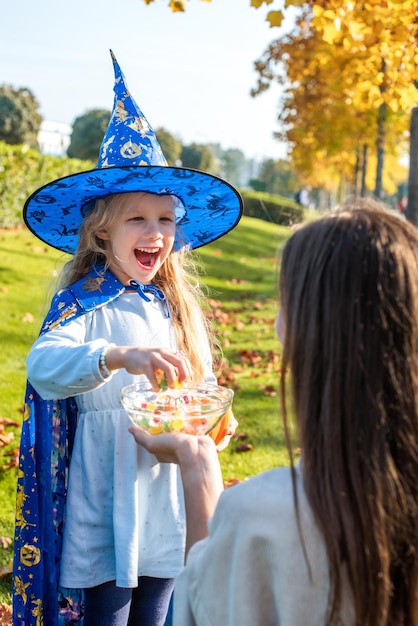 Une femme traite une fille habillée en sorcière avec des bonbons enfant prend des bonbons pour le tour ou le régal des vacances d'halloween