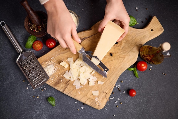 Une femme tranche un morceau de fromage dur parmesan italien traditionnel en flocons sur une coupe en bois