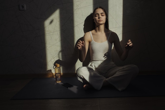 Femme tranquille au corps mince assise les yeux fermés dans la pose de Lotus ou Padmasana et méditant