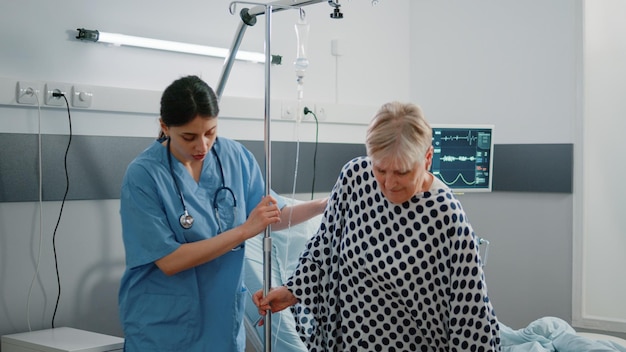 Femme travaillant comme infirmière aidant un patient malade dans une salle d'hôpital. Assistant médical aidant une personne malade avec un sac intraveineux pour la marche. Spécialiste de l'accompagnement d'un adulte