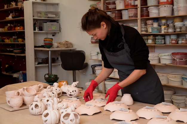 Femme travaillant dans un atelier de poterie faisant des bougeoirs en céramique avec forme de citrouille pour Halloween cel