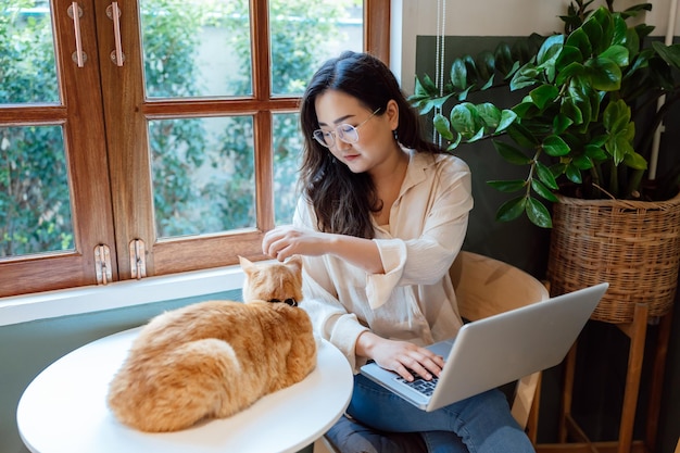 Femme travaillant à domicile avec chat chat endormi sur le clavier d'ordinateur portable assistant chat travaillant sur ordinateur portable