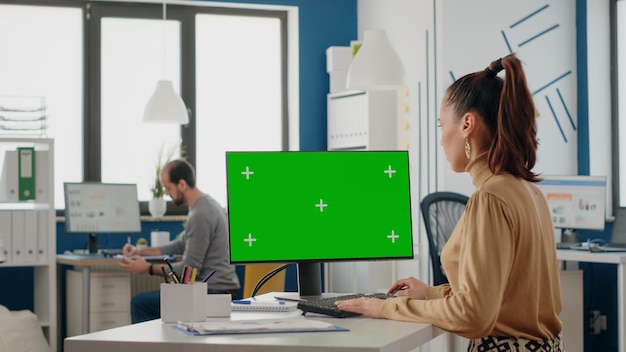 Femme travaillant avec un écran vert isolé sur un moniteur au bureau, regardant l'arrière-plan de la clé de chrominance avec un modèle de maquette à l'écran. Personne utilisant la clé chroma sur ordinateur dans le bureau d'affaires