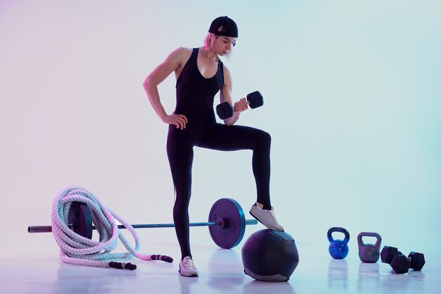 Femme travaillant avec des haltères femme entourée d'équipement de sport