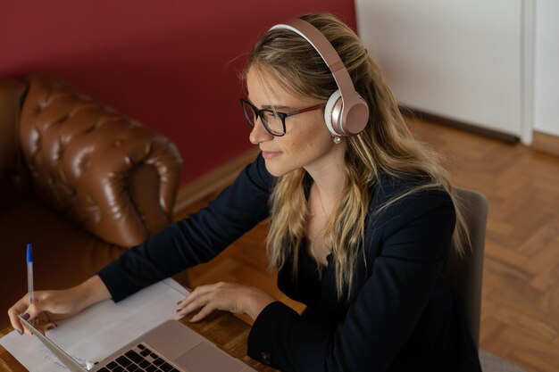 Femme travaillant à la maison avec un ordinateur portable et des papiers sur le bureau et des écouteurs bureau à domicile cahier gris