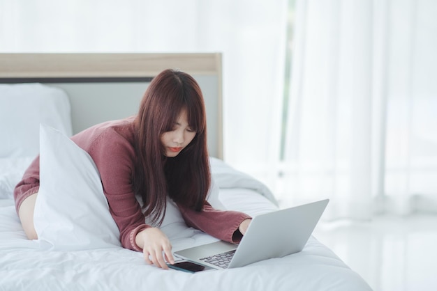 Femme travaillant sur un ordinateur portable assis sur le lit dans la maison.