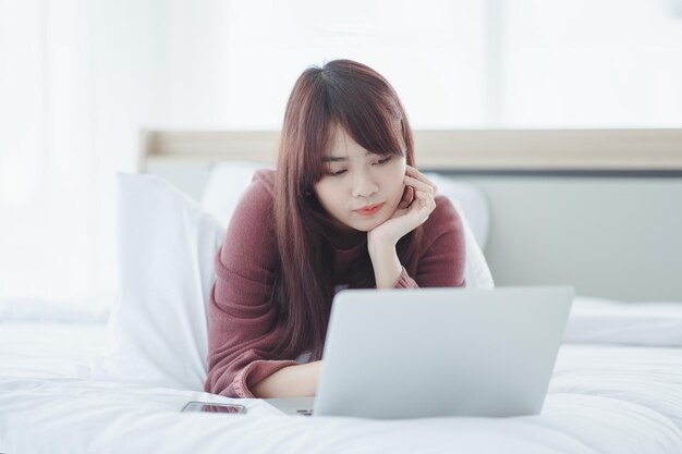 Femme travaillant sur un ordinateur portable assis sur le lit dans la maison.