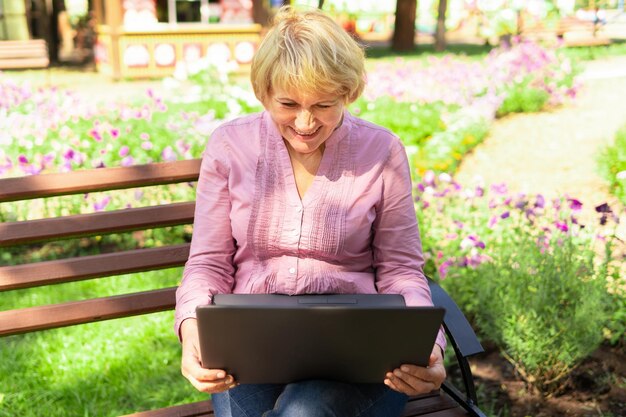 Une femme travaillant avec un ordinateur portable sur un banc de parc Femme d'âge moyen pigiste Elle étudie les médias sociaux par e-mail Elle est nerveuse