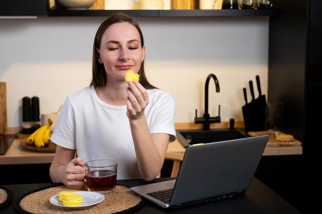 Femme travaillant sur un ordinateur portable dans un bureau à domicile une fille mange du gâteau et boit du thé dans la cuisine