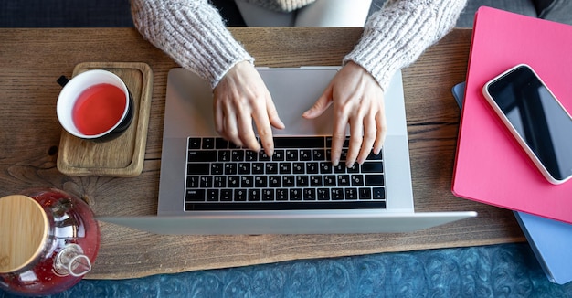 Femme travaillant sur un ordinateur portable dans un café avec une tasse de thé vue de dessus