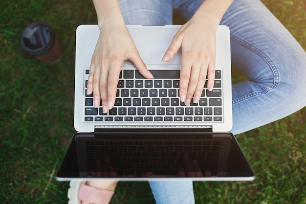 Femme travaillant sur ordinateur portable avec écran blanc, assise sur l'herbe verte à l'extérieur, vue de dessus