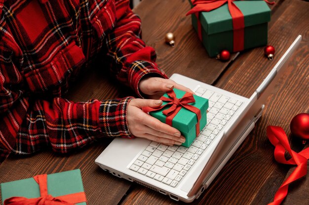 Femme travaillant avec un ordinateur portable et emballant des coffrets cadeaux sur une table.