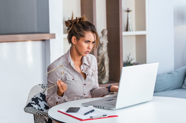 Femme travaillant avec un ordinateur portable à la maison, expression frustrée.