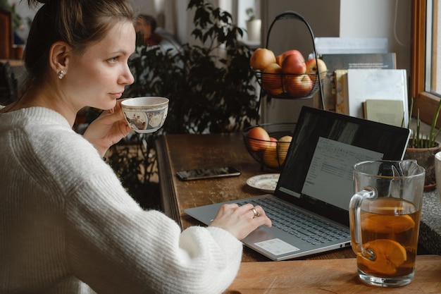 Femme travaillant avec un ordinateur portable par fenêtre à la maison