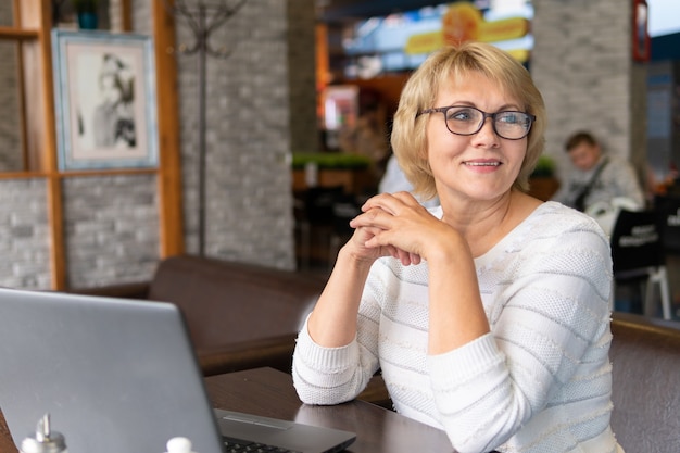 Une femme travaillant avec un ordinateur portable à une table dans un café. La femme travaille à distance. Elle regarde dans l'objectif