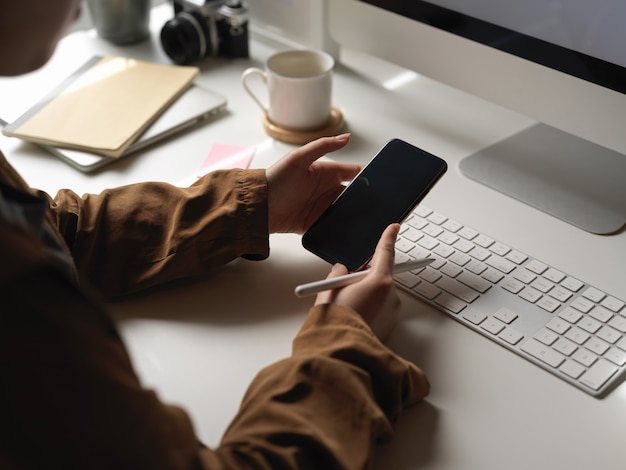 Femme travaillant avec un ordinateur tout en recherchant des informations sur un smartphone sur un bureau blanc