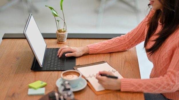 Femme travaillant en tapant sur une tablette numérique sans fil avec clavier tout en vérifiant la liste sur son journal