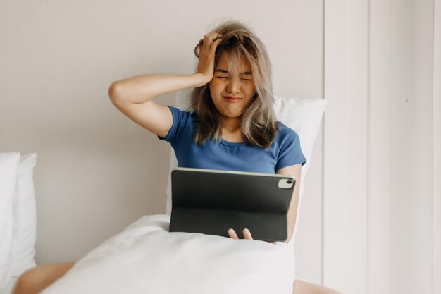 Une femme travaille en ligne sur son lit se sentant fatiguée en vacances.