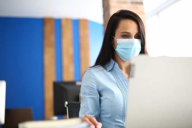 Femme travaille à l'ordinateur dans un masque médical de protection.