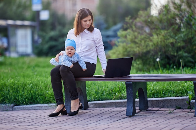 Une femme travaille avec un ordinateur portable avec un bébé sur les genoux à l'extérieur