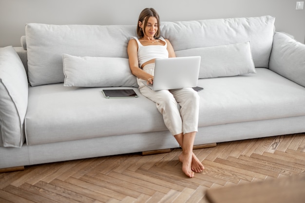 La femme travaille avec l'ordinateur portable sur le divan confortable