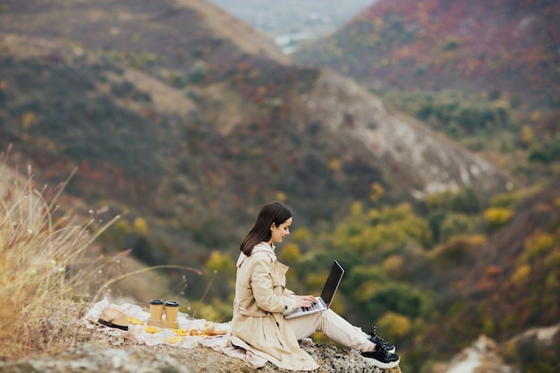 femme travaille sur un ordinateur portable sur un rocher dans la nature