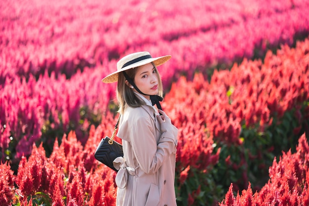 Femme en trench-coat et chapeau de paille marchant dans le champ de fleurs rouges.