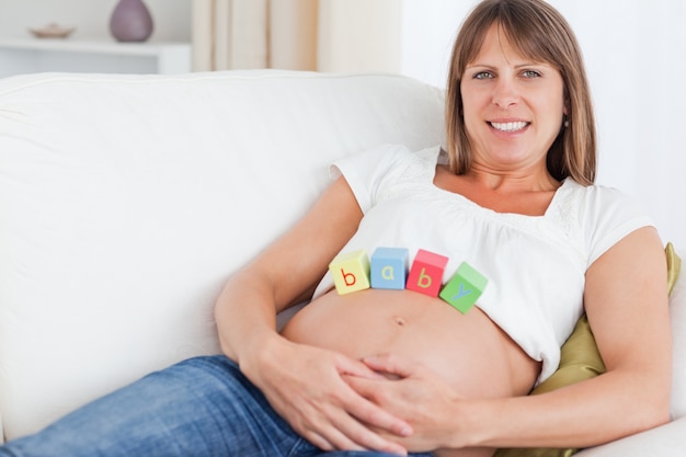 Femme très enceinte jouant avec des blocs de bois en position couchée sur un canapé