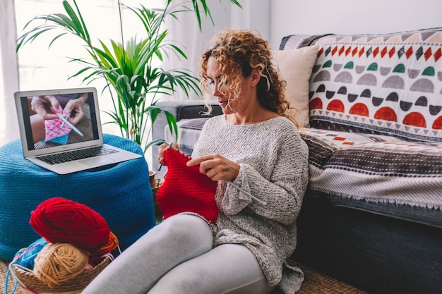 Une femme à tricoter confortable suit le didacticiel en pull chaud d'hiver tricoté et en pyjama aime travailler sur une couverture à carreaux rouge à carreaux à la maison en hiver confortable. Mode de vie intérieur gens heureux loisirs