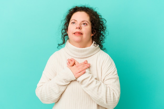 La femme trisomique isolée a une expression amicale, pressant la paume de la main contre la poitrine. Concept d'amour.