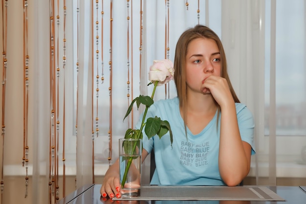 Femme triste assise à table avec une rose solitaire