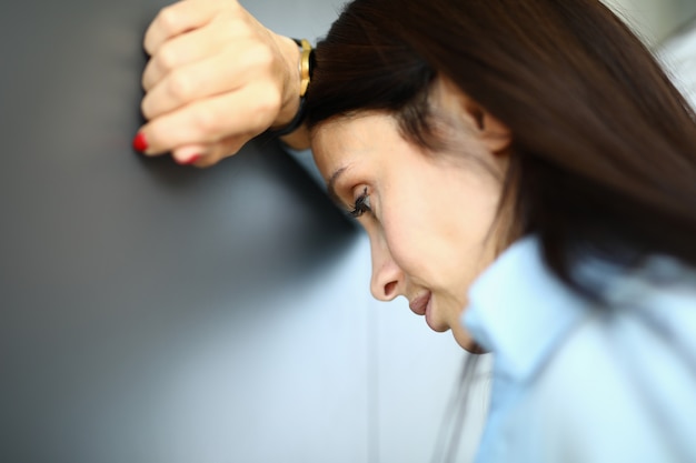 Femme triste est debout contre le mur avec son coude sur son bras