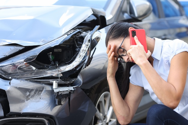 Femme triste parlant au téléphone portable près du concept de conduite de femme de voiture cassée