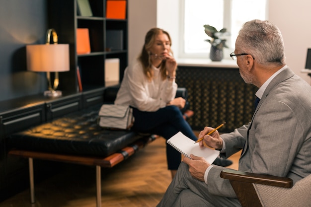 Femme triste réfléchie assise sur le canapé dans son bureau de psychanalystes tout en pensant et en détournant les yeux