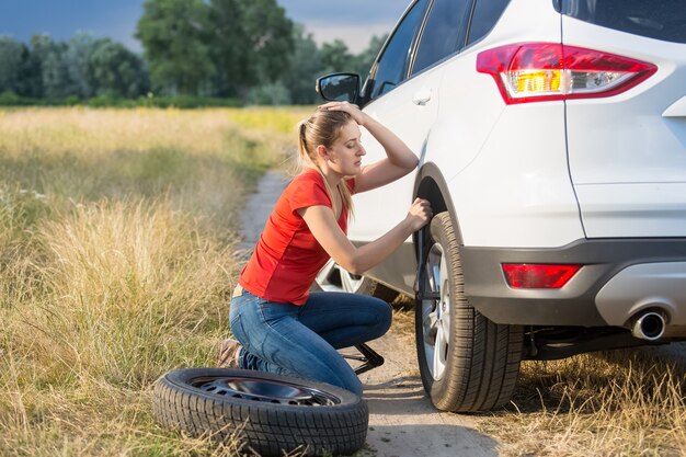 Femme triste remplaçant le pneu crevé de voiture sur le terrain