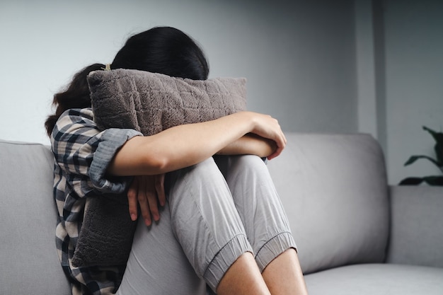 Une femme triste et solitaire malheureuse est assise sur le canapé et cache son visage sur un oreiller, concept de dépression