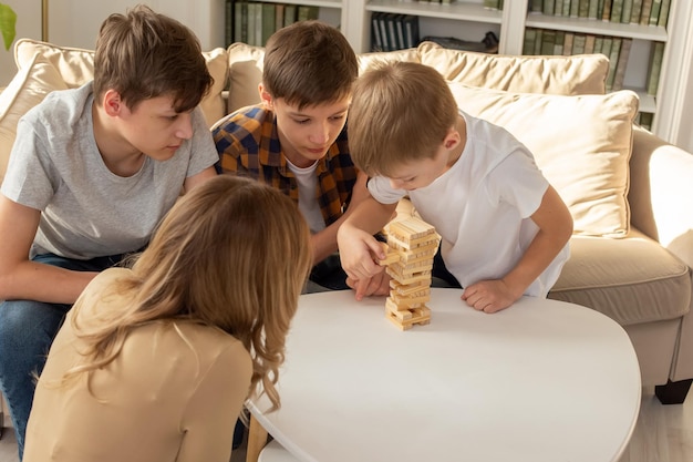 Une femme et trois garçons jouent avec enthousiasme à un jeu de société composé de blocs rectangulaires en bois