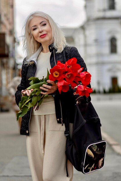Une femme avec des tulipes rouges se promène dans la ville et profite de la vie et du printemps