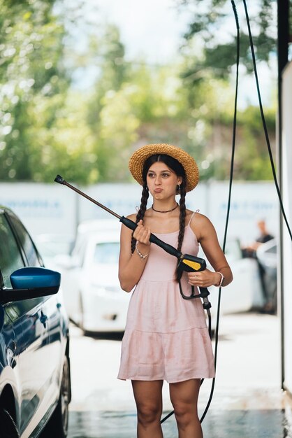 Femme avec tuyau haute pression au lavage de voiture