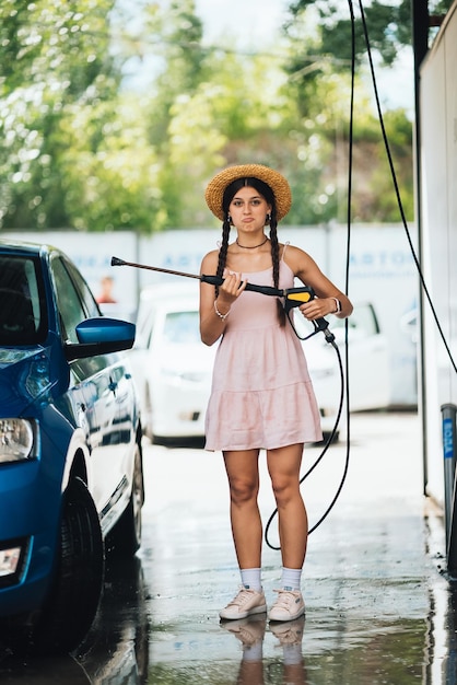 Femme avec tuyau haute pression au lavage de voiture