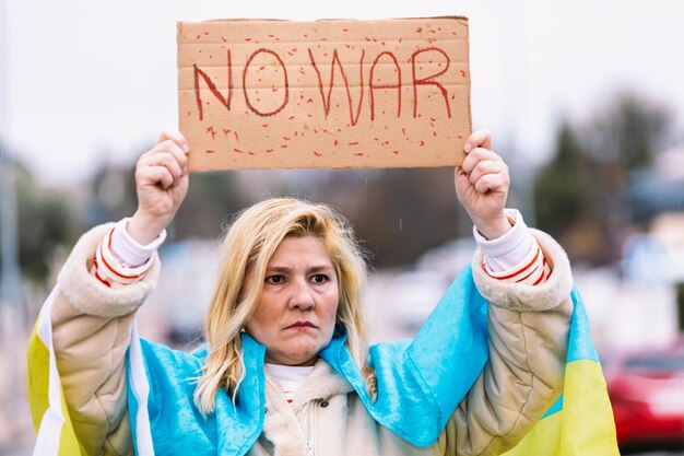 Femme ukrainienne aux cheveux blonds et au geste sérieux avec un drapeau ukrainien bleu et jaune avec un panneau indiquant 39No War39 dans la rue pour protester contre la guerre UkraineRussia