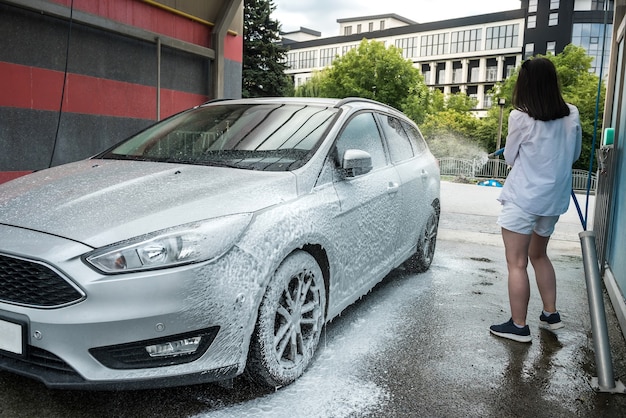 Femme ukrainienne avec pistolet à eau en mousse nettoie sa voiture en service