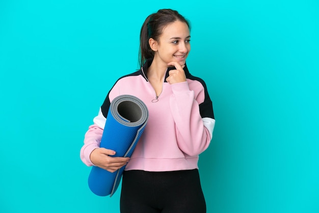 Femme ukrainienne sportive allant à des cours de yoga tout en tenant un tapis regardant sur le côté et souriant