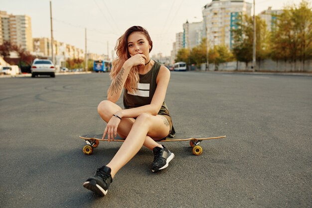 Femme urbaine assise sur Longboard sur la place de la ville