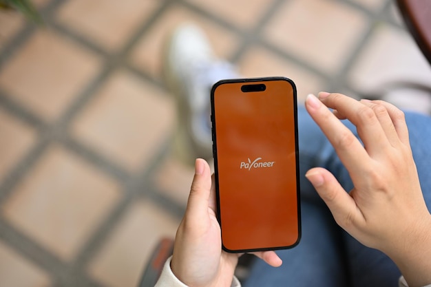 Une femme utilisant l'application Payoneer sur son téléphone iPhone avec le logo Payoneer à l'écran