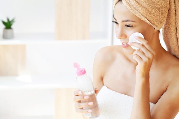 Femme utilisant une crème hydratante adoucissante avec un coton sur son visage enlevant des cosmétiques