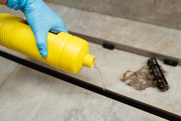 Femme utilisant des déboucheurs liquides pour nettoyer le drain de douche