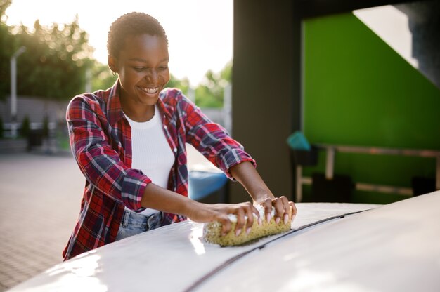 Femme utilisant une éponge avec de la mousse, station de lavage de voiture à la main. Industrie ou entreprise de lavage de voitures. La personne de sexe féminin nettoie son véhicule de la saleté à l'extérieur